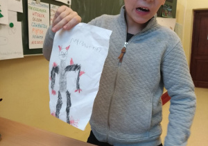 Uczeń pokazujący narysowanego robota, który składa się z trójkątów i prostokątów